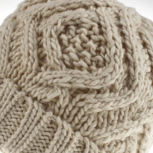 Macro detail of the chunky cable knit texture on this soft beige winter beanie