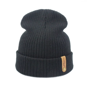 Close-up of black ribbed knit beanie featuring a brown leather Masswee label and gold rivet