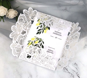 Detail of laser-cut white wedding invitation with lemon pattern and floral backdrop