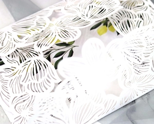 Detailed close-up of white laser-cut floral wedding invitation with inner card