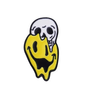 Détail d'un pin's en émail souriant jaune fondant montrant un crâne de dessin animé