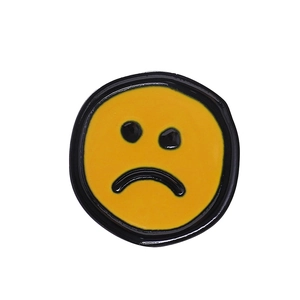 Gros plan d'un badge rond en métal jaune avec un emoji visage triste qui pleure