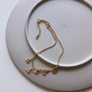 Close-up of minimalist gold star charms on a 925 silver anklet over a grey tray