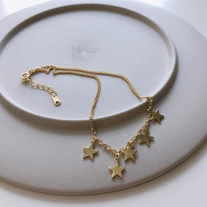 Detail of a minimalist gold star anklet in 925 silver on a gray decorative plate