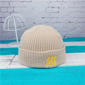 Detail of beige ribbed knit beanie featuring unique yellow embroidery on the folded brim
