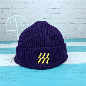Dark purple ribbed knit beanie with yellow embroidered logo on a blue wood surface