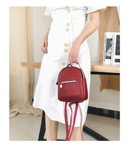 Detail of wine red mini backpack with pebbled leather texture and gold hardware