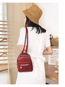 Detail view of a small dark red PU leather backpack with gold zippers and metal charm