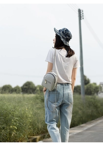 Outdoor shot of a grey mini leather backpack with gold zippers shown on a model's back
