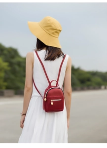 Detail of red mini backpack with golden zipper and metal charm on a white dress