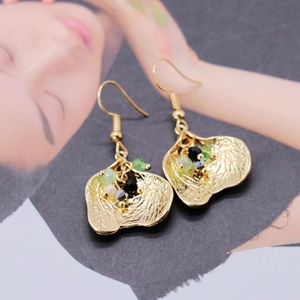 Macro detail of gold leaf drop earrings featuring colorful beads on artistic magazine background