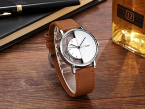 Detail of TOMI hollow dial watch with brown leather strap and silver case on a desk