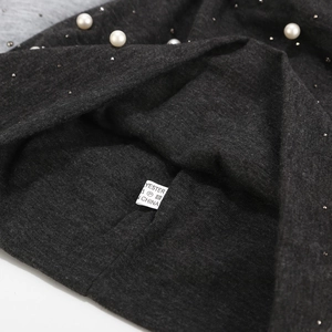 Detail of dark grey knit fabric featuring white pearls and sparkling rhinestone studs