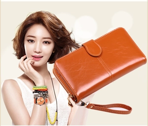 Elegant woman holding a glossy orange leather long wallet with wristlet strap and zipper