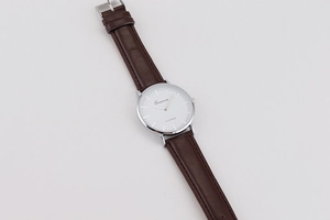 Detailed macro view of the minimalist white watch dial with silver markers and brown leather strap