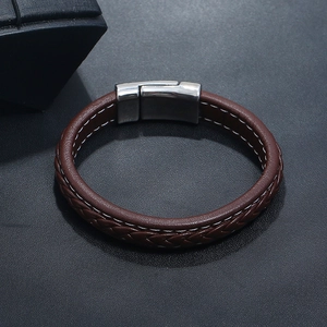 Détail d'un bracelet en cuir tressé marron avec fermoir magnétique argenté sur fond noir