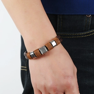 Men's brown braided leather bracelet with silver metal charms worn by a model