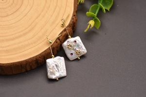 Detail shot of baroque pearl earrings with crystal accents on a rustic wooden stand.