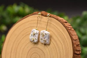 Close-up of Baroque pearl earrings with sparkling crystal inlays and gold metal finish.