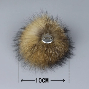 Detail of 10cm raccoon fur pom pom with metal pin base on dark background