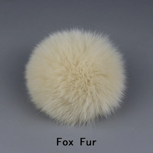 Detail view of large cream-colored fox fur pompom accessory with fluffy texture