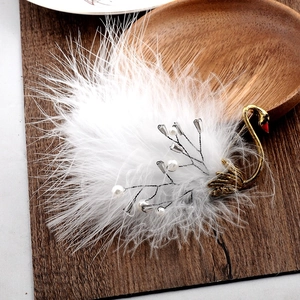 Detailed close-up of a white ostrich feather swan brooch with gold metal and pearls