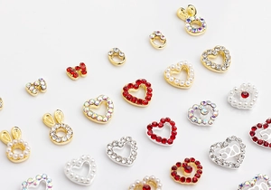 Macro view of gold and silver heart-shaped nail art charms with red rhinestones and pearls