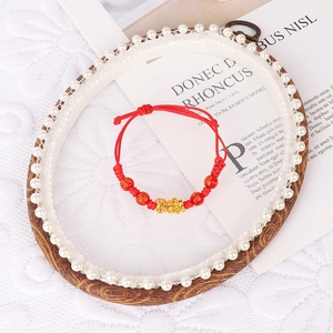 Detail of red braided bracelet with golden Pixiu charm and patterned beads on lace