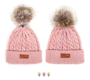 Détail du bonnet en tricot rose montrant le pompon amovible avec bouton pression et écusson