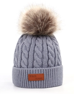 Gros plan sur bonnet en tricot bleu clair avec motifs torsadés et pompon en fausse fourrure
