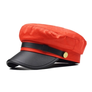 Detail of red fabric newsboy hat with black leather brim and golden metal button