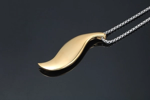 Close-up of gold S-shaped leaf pendant on silver chain over a black reflective surface