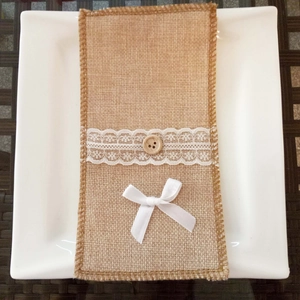 Detail of burlap cutlery holder with white lace and bow on a white plate