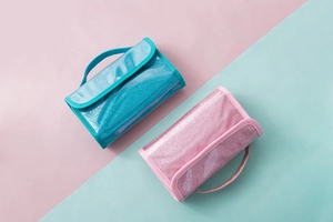 Pink and blue glitter PVC toiletry bags with handles on a matching pastel background