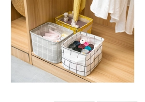 Foldable cotton linen storage bins with grid patterns inside a wooden wardrobe shelf