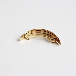 Detail of golden metal hair clip featuring a curved minimalist design and textured stripes
