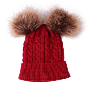 Detailed knit texture of red baby winter hat featuring two large brown faux fur pom poms
