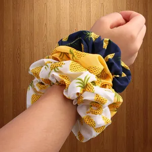 Three-piece pineapple print scrunchies in white, yellow and navy worn on a wrist