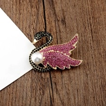 Detail of a swan brooch with pink and black crystals and a white pearl on a wood surface