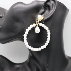 Detail of elegant gold hoop earrings with white faux pearls on a black display model