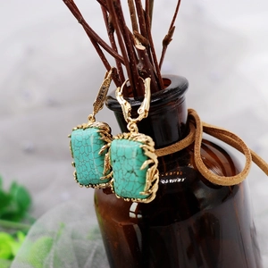 Detailed shot of rectangle turquoise earrings with gold frame on a vintage dark bottle