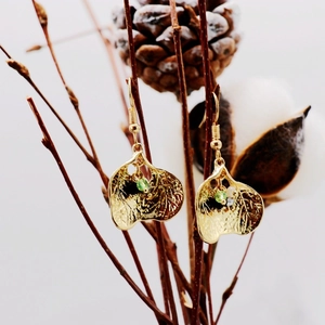 Macro shot of gold leaf-shaped earrings with green crystals hanging on a rustic branch