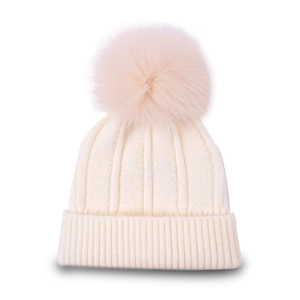 Detailed close-up of cream knit beanie featuring a large fluffy faux fur pom-pom topper