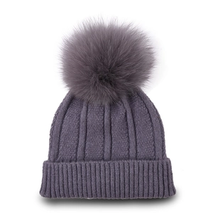 Detail of dark grey knit beanie featuring a large fluffy faux fur pompom and ribbed texture