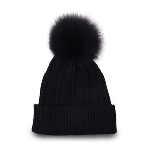 Detail of black ribbed knit beanie featuring a large fluffy faux fur pom-pom on top