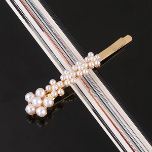 Detail shot of golden hair clip with clusters of white pearls on a sleek black background