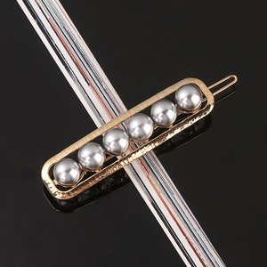 Detail of a golden metal hair clip with grey pearls on a reflective black background