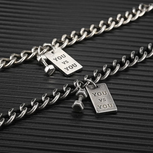 Dettaglio macro delle collane con manubrio e incisione YOU VS YOU in acciaio argento e grigio