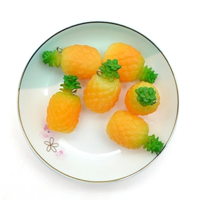 Realistic PVC pineapple keychains with green leaves and golden metal rings in a ceramic bowl