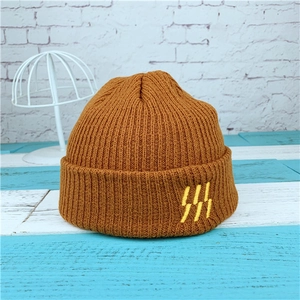Detail of a brown knitted beanie showing the ribbed texture and yellow abstract embroidery